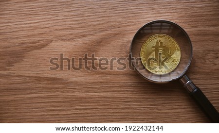 A magnifying glass magnify the replica of gold bitcoin on wooden background with copy space.
