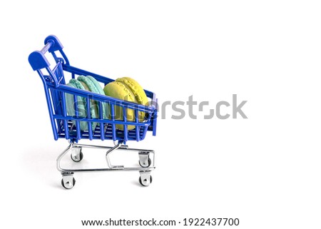 Blue and yellow macarons lie in metal shopping cart isolated on white background. High quality photo