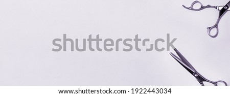 Banner flat lay from above of professional silver hair cutting shears set on purple background. Hairdresser salon equipment and haircut work tools concept during quarantine with copy space.