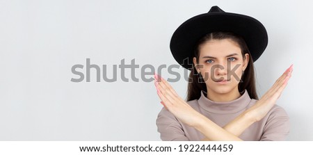 Serious Young brunette woman keeps two arms crossed, makes stop or ban gesture, indicates that the passage is closed, denial concept. Studio shot, white background