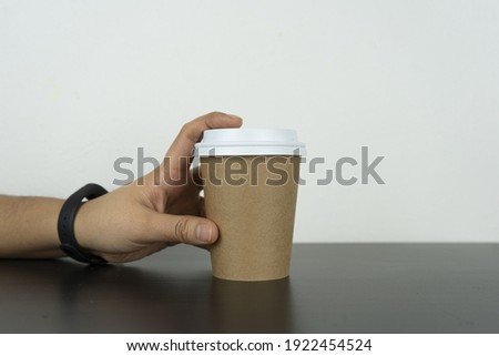 A hand grabs the take-away paper cup on a black table. This photo is suitable for use as a mockup to put your logo or design