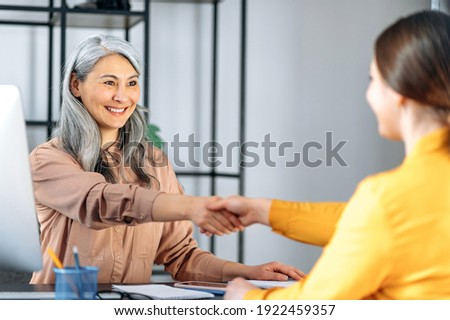 An asian mature gray-haired friendly business woman, is shaking hands with woman jobseeker. Successful middle aged lady making deal with female business partner Royalty-Free Stock Photo #1922459357