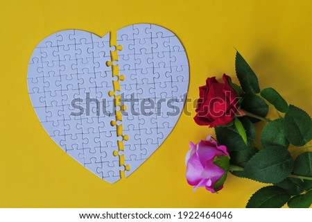 Jigsaw puzzle the shape of a heart detached in the middle with a couple of roses