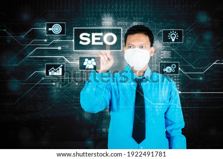 Picture of businessman wearing face mask while touching SEO button on the virtual screen