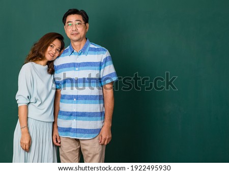 Portrait of a smiley happy loving Asian couple dressed casually standing relaxedly, smiling to a camera for studio shot over green background. Warmth family concept.