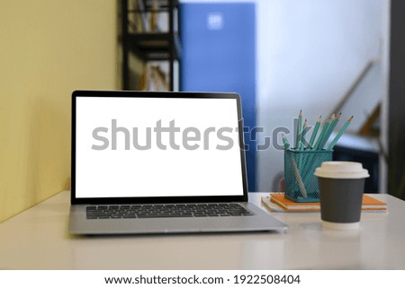 Close up view of computer laptop with blank screen, coffee cup and pencils holder on white office desk.