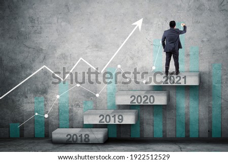 Back view of businessman drawing upward arrow and growth chart while standing on the stair with numbers 2021 Royalty-Free Stock Photo #1922512529