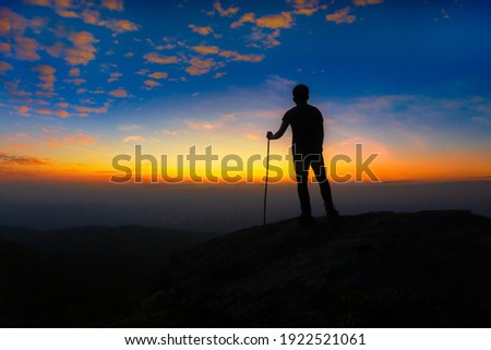 Man stands on the edge of sandstone cliff and watching over misty valley to Sun. Beautiful moment the miracle of nature