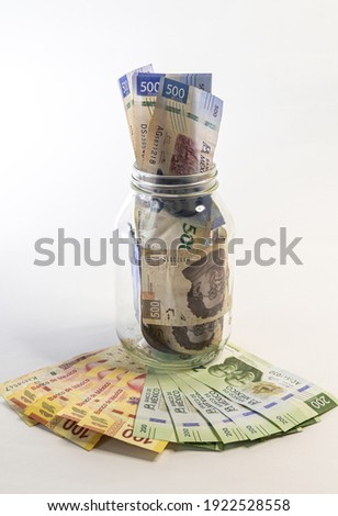 Some bills of 500 mexican pesos in a jar of glass over another bills.