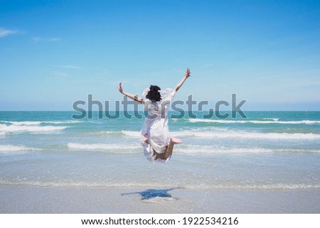 Happy young lady are jumping, feel relax, fun, and enjoy holiday at tropical coast beach with clear cloud and blue sky background