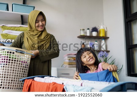 muslim asian mother and child girl little helper in laundry room near washing machine Royalty-Free Stock Photo #1922552060