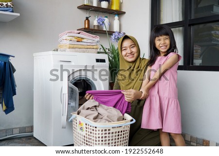 muslim asian mother and child girl little helper in laundry room near washing machine Royalty-Free Stock Photo #1922552648