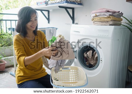 woman in front of the washing machine doing some laundry loading clothes inside
