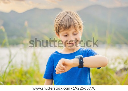Boy uses kids smart watch outdoor against the background of the garden