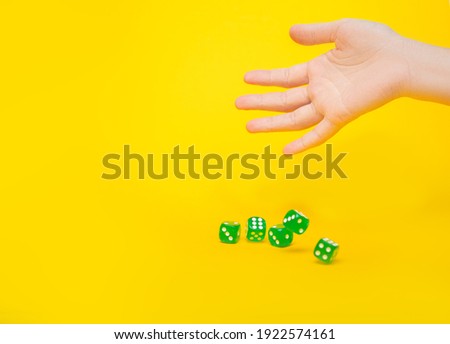 A lot of green dice fall from the hand on a yellow background with space for text: board games, selective focus on the hand, a photo in motion