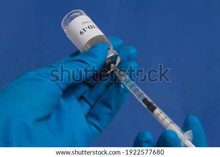 Hands of a doctor or nurse in blue medical gloves drawing a syringe with covid-19 vaccine from a vial, close up. Coronavirus vaccination concept.