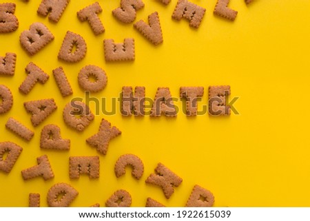 Word Hate in the middle of the picture made of tasty crunchy cookies in form of English alphabet letters, textured bright yellow background, health, dieting and medical concept. Copy space big letters