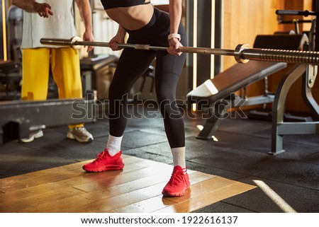 Cropped photo of a fit young woman in black leggins working out with a barbell