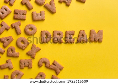 Word Dream in the middle of picture made of tasty crunchy cookies in form of English alphabet letters, textured bright yellow background, health, dieting and medical concept. Copy space, big letters