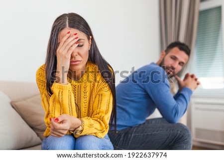 Sad pensive young girl thinking of relationships problems sitting on sofa with offended boyfriend, conflicts in marriage, upset couple after fight dispute, making decision of breaking up get divorced Royalty-Free Stock Photo #1922637974