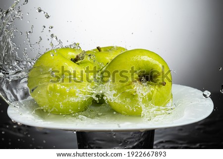 whole green apple on a white plate with splash and water flow