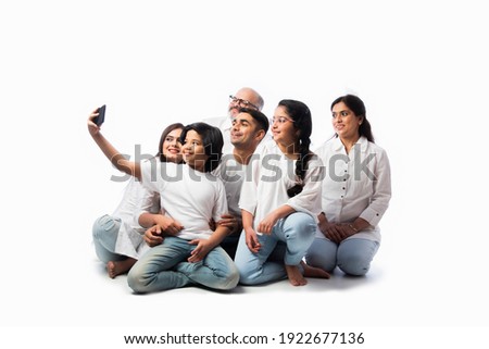 Indian family of six video calling on smartphone or taking selfie picture against white
