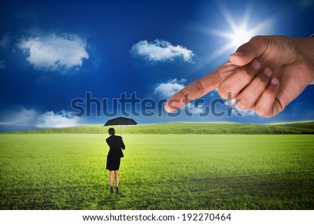 Giant hand pointing at young businesswoman holding umbrella against sunny green landscape