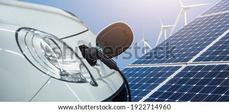 Close up of electric car with a connected charging cable on the background of solar panels and wind turbines - sources of clean renewable energy Royalty-Free Stock Photo #1922714960