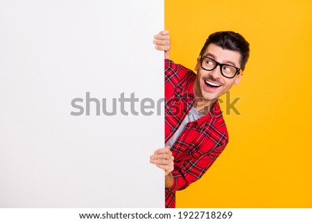 Photo of funny funky young man wear red checkered shirt arm eyewear looking billboard empty space isolated yellow color background