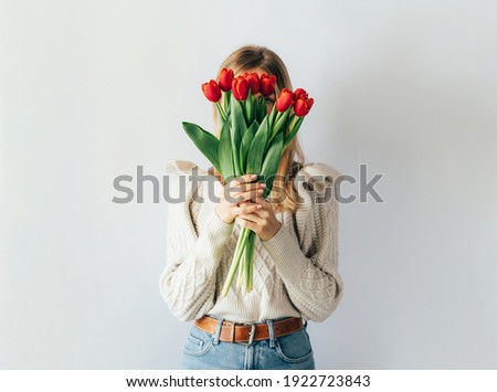 Portrait of a stylish young woman hiding her face with a bouquet of red tulips. Royalty-Free Stock Photo #1922723843