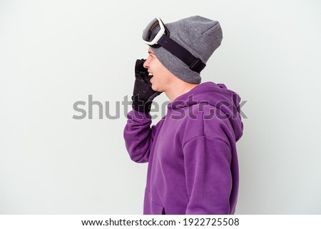 Young man holding a snowboard board isolated on white background shouting and holding palm near opened mouth.
