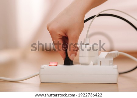 Woman pluging the wire into white extension cord. Close up of female hand put cabel Royalty-Free Stock Photo #1922736422