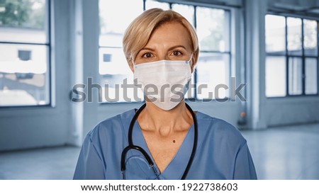 Mature doctor in medical mask looking at camera in hospital Royalty-Free Stock Photo #1922738603