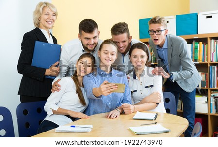 Cheerful students of different age doing group selfie on smartphone in classroom