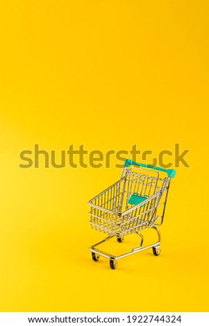 Metallic shopping cart trolley on yellow color background with copy space. Shopping symbol.