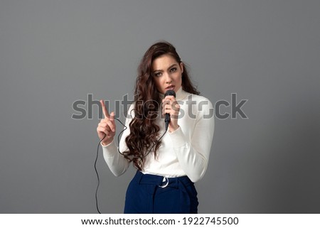 attractive female conference speaker during presentation, holds microphone and makes some gestures, isolated on gray Royalty-Free Stock Photo #1922745500