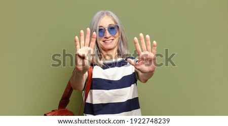 senior woman smiling and looking friendly, showing number nine or ninth with hand forward, counting down