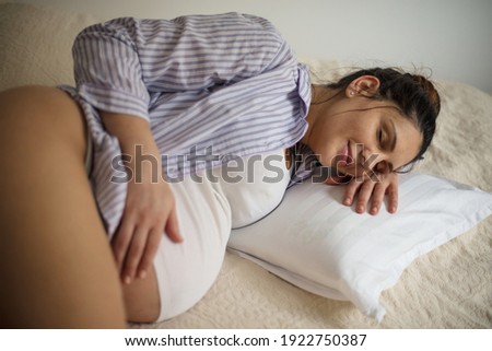 Pregnant woman sleeping on bed and touching her belly. 