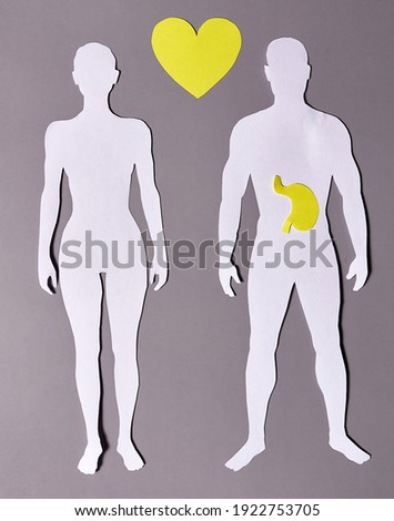 A paper silhouette of a man and woman with a yellow stomach and heart on a gray background.