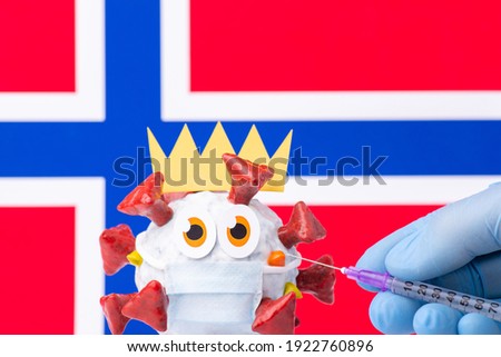 Nurse holding syringe with vaccine against coronavirus. Handmade afraid cartoon coronavirus model in front of Norway flag.