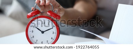 Woman sleep in bed. Man want to turn off alarm in dream. Ringing alarm clock. On table there is closeup alarm clock and open book lye. Be late for work concept.