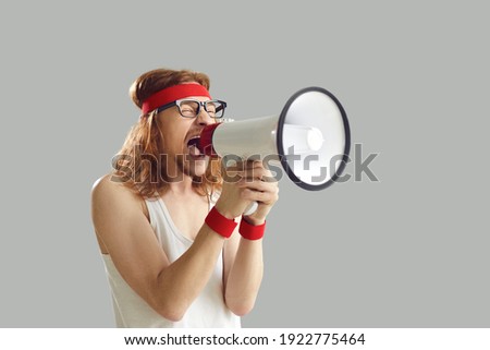 Funny noisy crazy nerdy young man in retro sportswear standing isolated on gray background, yelling in megaphone, announcing important marketing message, advertising gym workout equipment sale