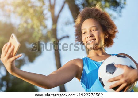 Cute little girl with soccer ball making selfie outdoors