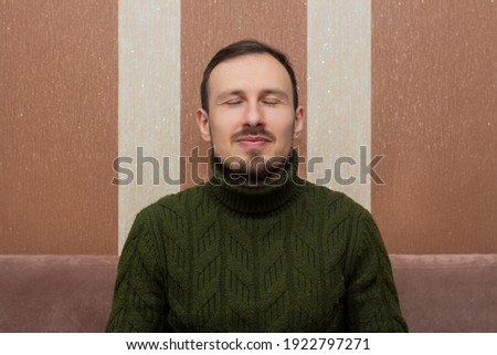 Male portrait, a man in a green sweater with his eyes closed sitting on a sofa on a striped background