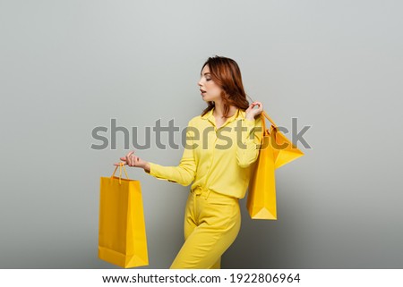 curly woman in yellow clothes holding shopping bags on grey
