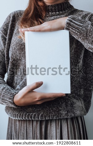 Woman holding stack of books, books closeup, blurry background