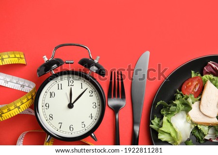 Plate of tasty salad, cutlery, alarm clock and measuring tape on red background, flat lay. Nutrition regime Royalty-Free Stock Photo #1922811281