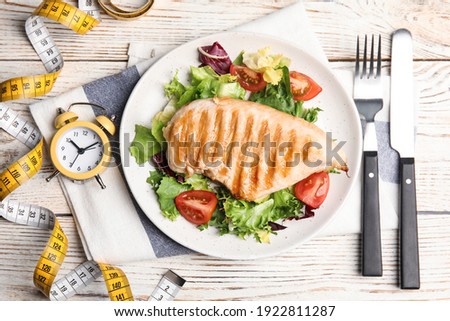 Plate of appetizing food, alarm clock and measuring tape on white wooden table, flat lay. Nutrition regime Royalty-Free Stock Photo #1922811287