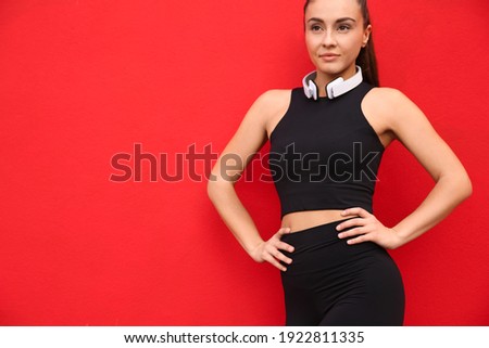 Young woman in sportswear with headphones on red background. Space for text