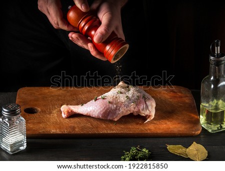 Cooking a chicken leg with the hands of a chef on dark background. Add pepper to chicken meat. Free advertising space for a restaurant